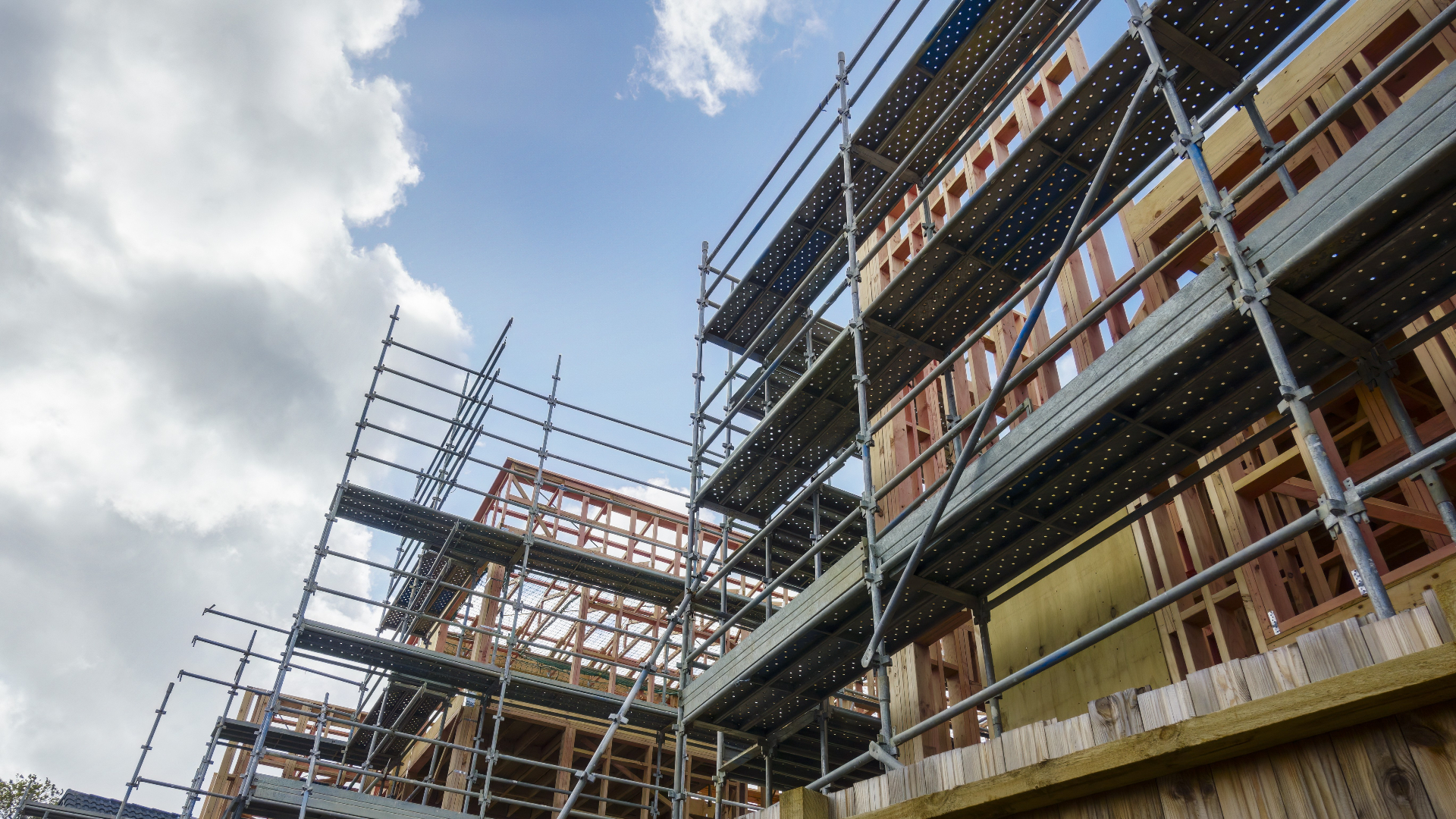 Timber frame construction site with scaffolding against a blue sky